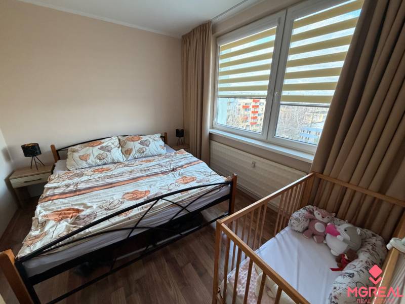 Bedroom in a 4-room apartment with a bed and a baby crib, floor with wooden decor.