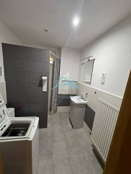 A bathroom in a family house with a shower, washing machine, and sink, furnished with tiles.
