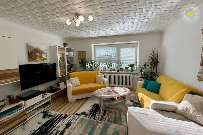 Living room in a two-room apartment with a wooden decor floor, a yellow sofa, and decorations.