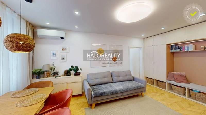Living room with a sofa, dining table, and wood-patterned floor in a three-room apartment.