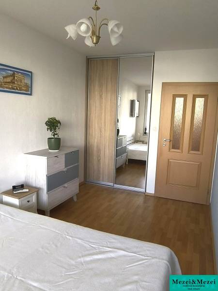 A bedroom in a two-room apartment with a wood-patterned floor, built-in wardrobe, and dresser.