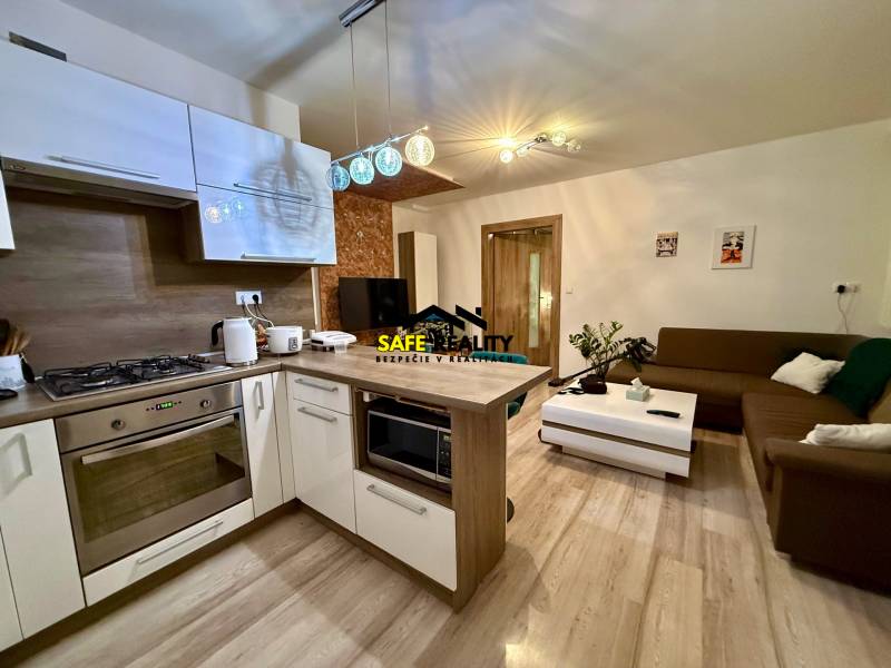 A kitchen connected to the living room in a two-room apartment, a floor with a wooden decor, a comfortable sofa.
