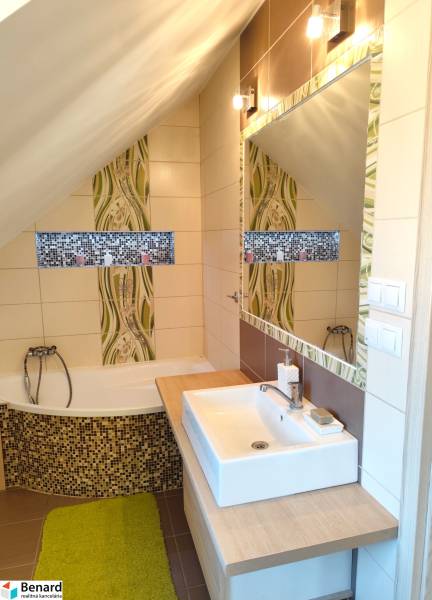 Bathroom in a family house with a bathtub, sink, mirror, and mosaic decoration.