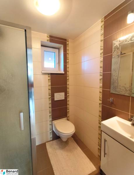 Bathroom in a family house with a toilet, shower, window, and tiles.