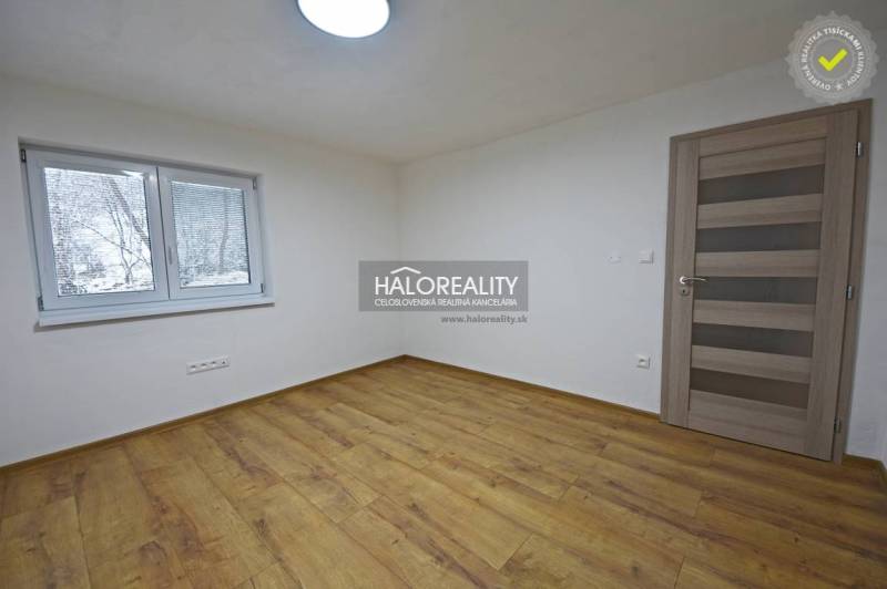 An empty room in a family house with a wood-patterned floor and a window.