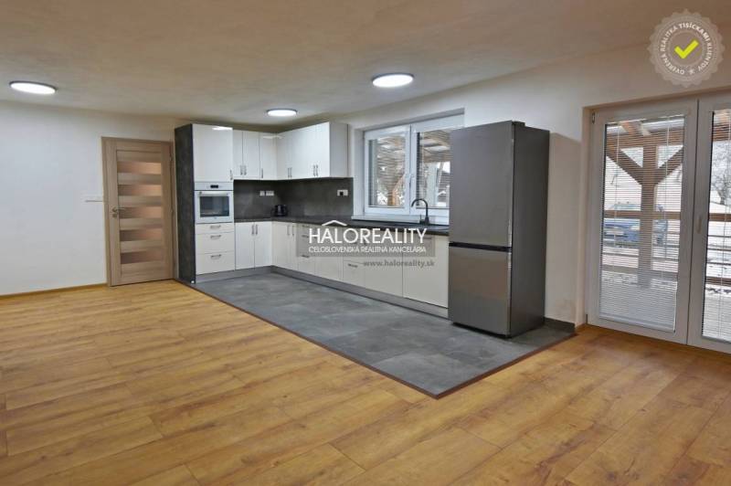 A kitchen in a family house with white cabinets, gray tiles, and a wooden decor floor.