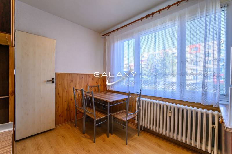 Dining nook in a 2-room apartment with a wood-patterned floor and a large window.