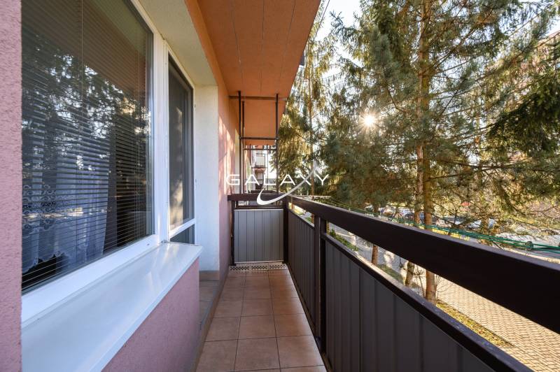 A balcony on Sládkovičova Street in Fiľakovo, surrounded by greenery, part of a 2-room apartment.