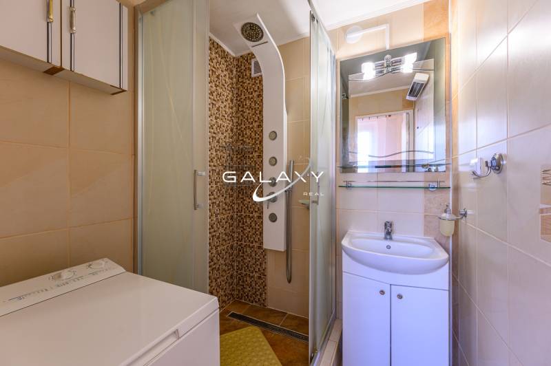 A bathroom with a shower, sink, and washing machine in a 2-room apartment.