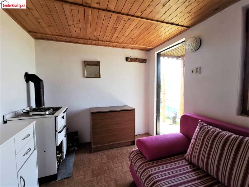 In a cozy cabin, there is a vintage stove, a wooden ceiling, and a comfortable upholstered couch.