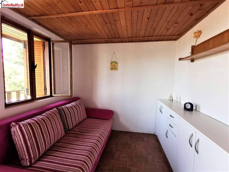 A cabin interior with a wooden ceiling, a comfortable couch, and white storage furniture.