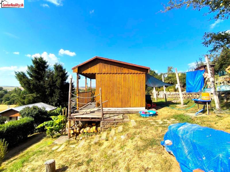 A wooden cabin in Partizánske surrounded by nature, with a grassy plot and outdoor seating.