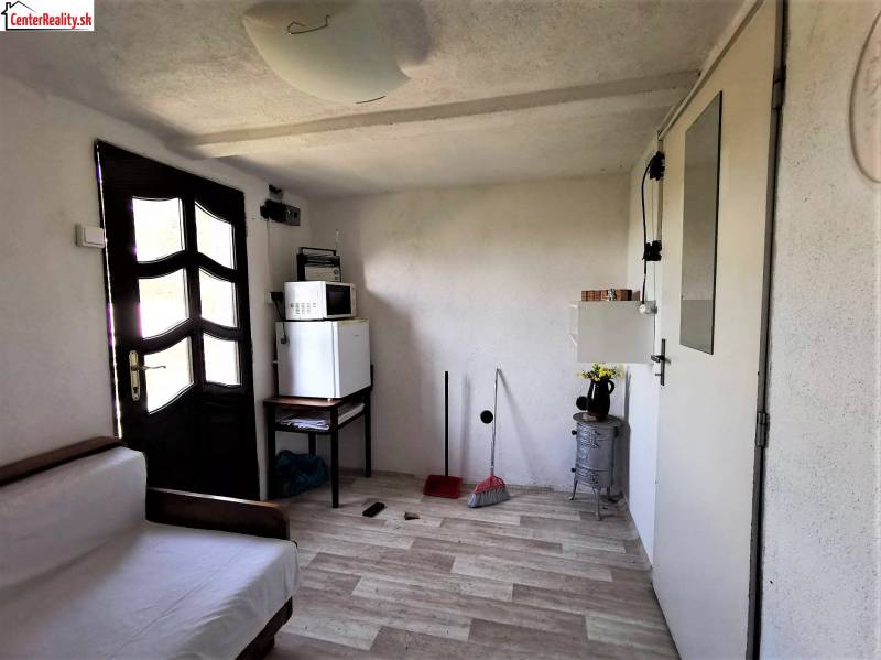 A room in a cottage with a sofa, fridge, microwave, and simple furniture.