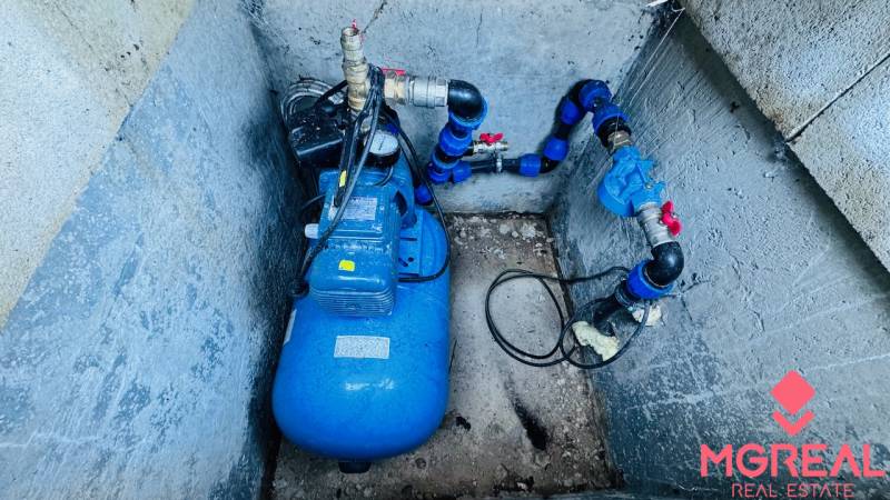 In a concrete pit, there is a blue pressure water pump system with piping.