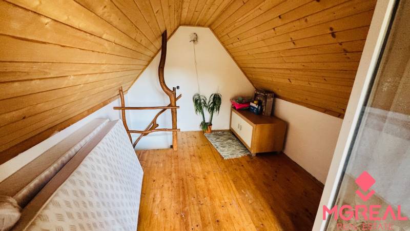 Attic space with a wooden decor floor and simple furniture in a cottage.
