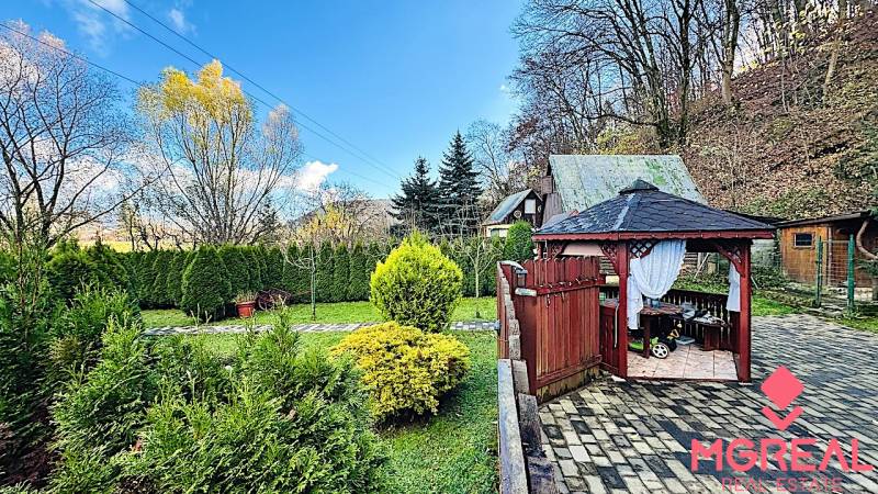 A garden by the cottage in Partizánske with a gazebo, trimmed bushes, and trees.