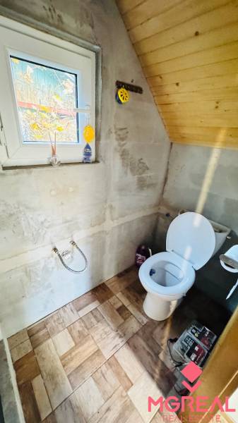 A toilet in a wooden cabin, with a wooden decor floor and a window.