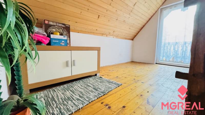 The attic of the cottage with a wooden decor floor, a cabinet, and a plant.