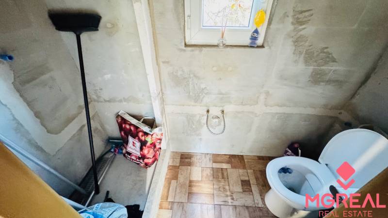 A bathroom in a cabin with a wooden decor floor, a toilet, and a window.