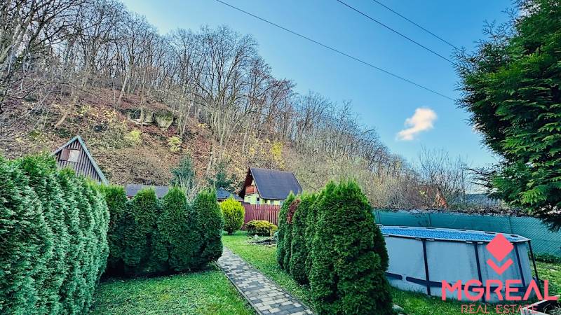 A garden by the cottage in Partizánske with a pool and trees under the hill.