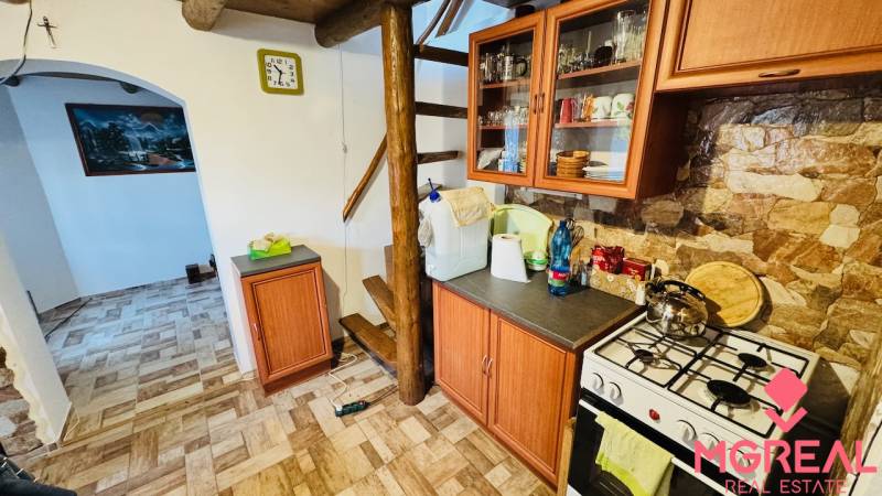 A kitchen in a cabin with wooden decor, stairs, appliances, and furniture with a stone wall.