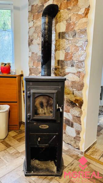 Wood-burning stove with a chimney, stone wall, wooden decor flooring in a cabin.
