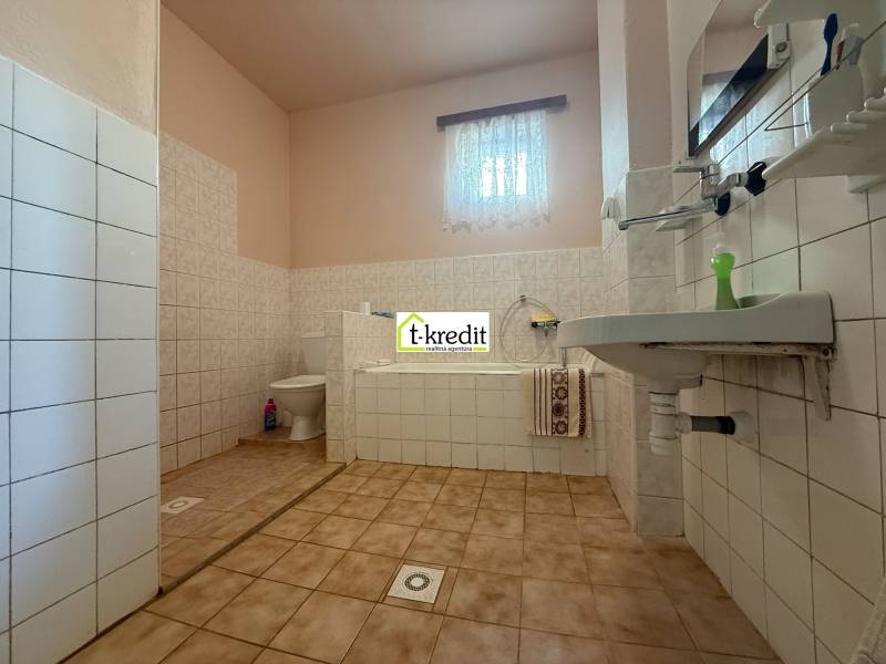 A bathroom with a bathtub and a sink in a family house with tiled flooring and light-colored walls.