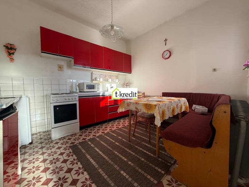 A kitchen in a family house with a red kitchen unit, a sofa, a dining table, and tiles.