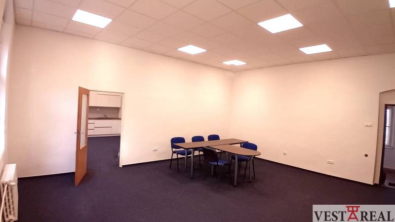 An office with blue chairs and tables, white wall, open door to a small kitchenette.