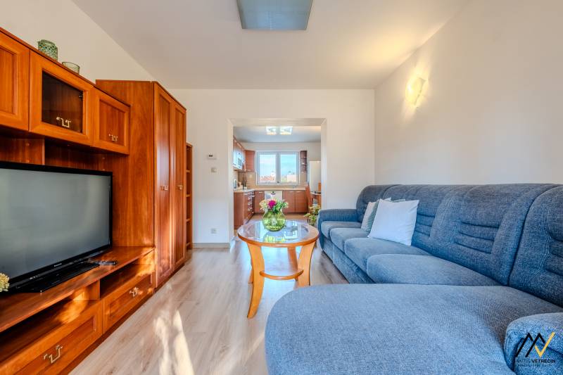 Living room in a two-room apartment with a wooden decor floor and a well-lit kitchen.