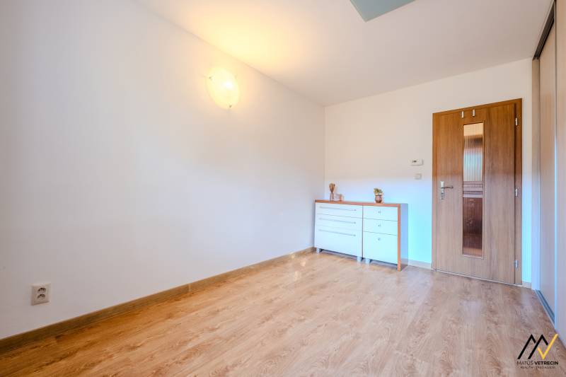 A room in a 2-room apartment with a wooden decor floor and a white dresser.