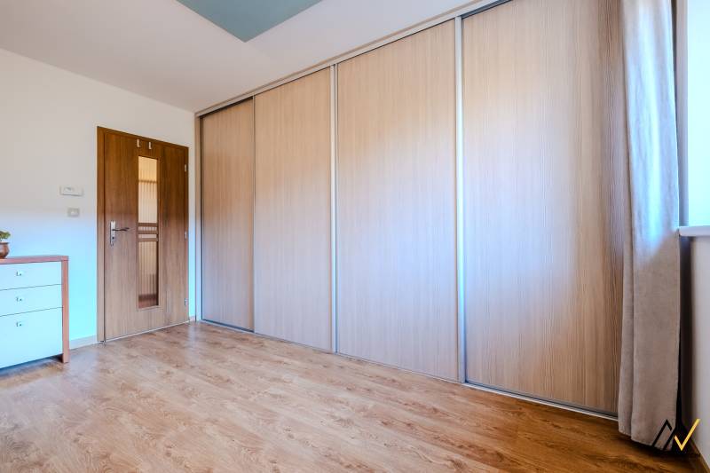 A room in a 2-room apartment with a wooden decor floor, a wardrobe, and a chest of drawers.