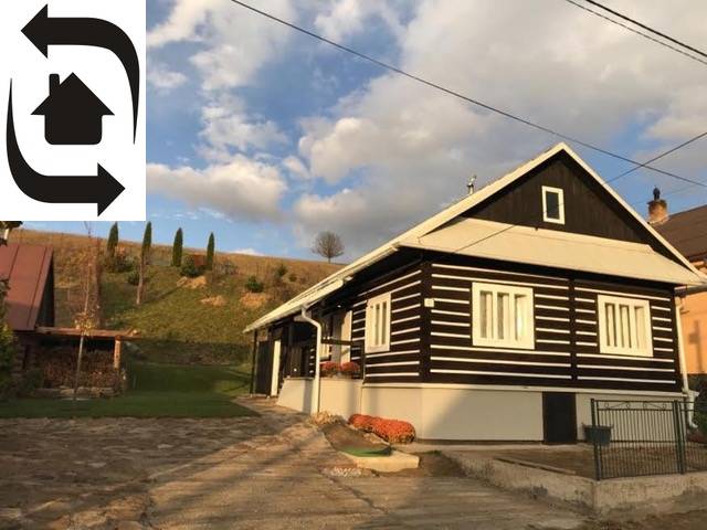 A cottage in Legnava with wooden cladding and a paved courtyard, surrounded by nature and hills.