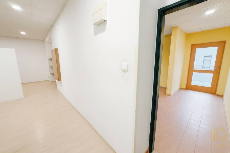 A white corridor in commercial premises with wood-patterned flooring and a room with tiles.