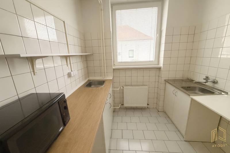 A kitchen space with white tiles, a microwave, and a wood-patterned floor.