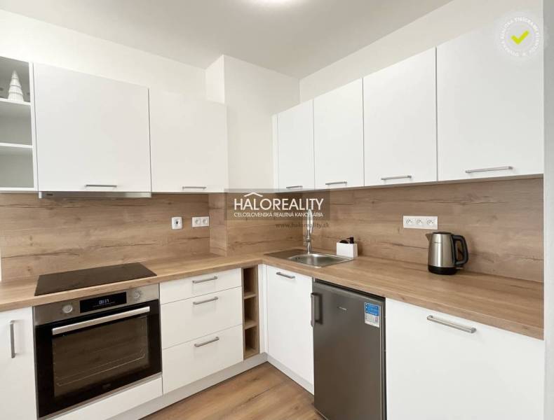 A kitchen in a studio apartment with a wood-patterned floor and white cabinets.