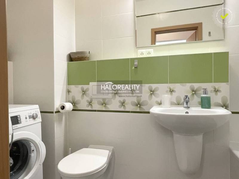 Bathroom in a studio apartment with a washing machine, sink, and green tiles.