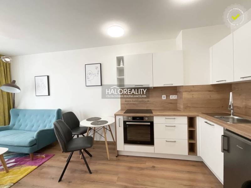 A kitchen in a studio apartment with a wood-patterned floor and light-colored furniture.