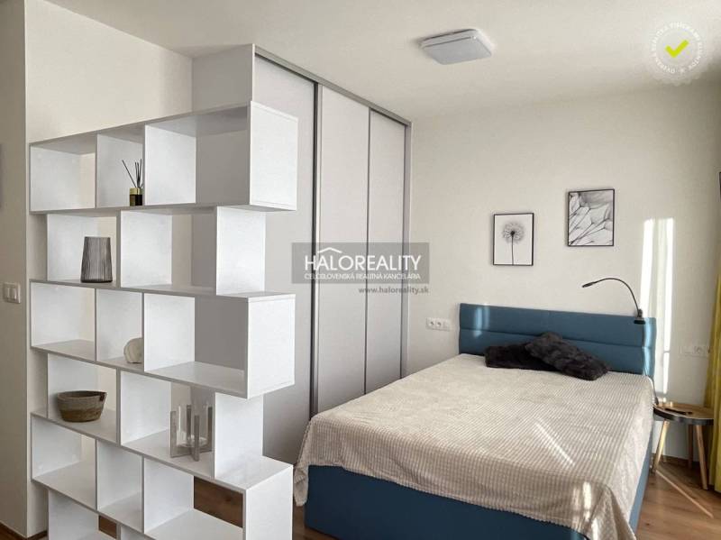 A bedroom in a studio apartment with a shelving partition and a floor bed with a wooden decor.