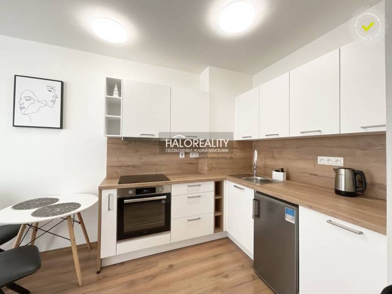 A kitchen in a studio apartment with light furniture and a wooden decor floor.