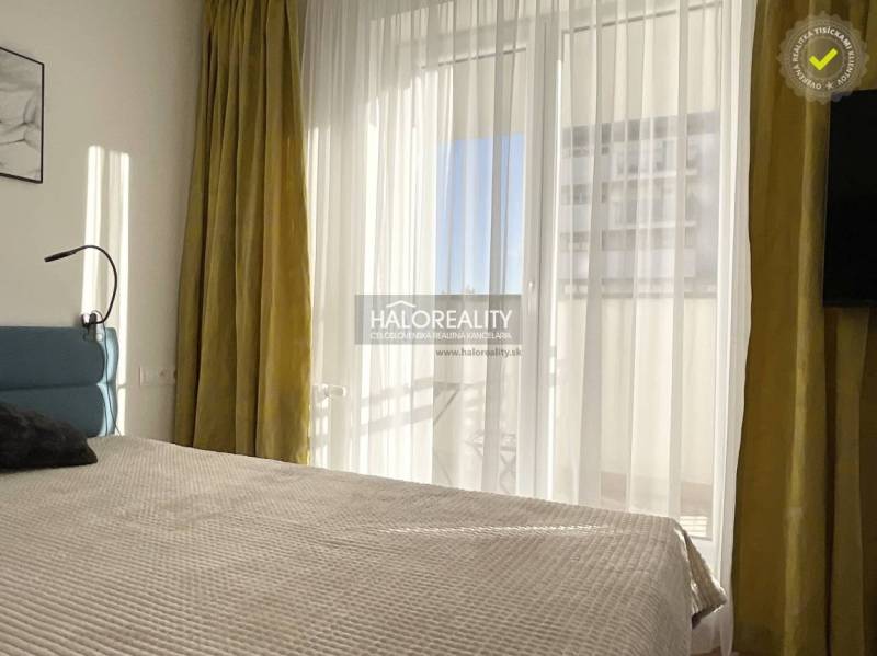 Bright bedroom in a one-room apartment with a large window and curtains.