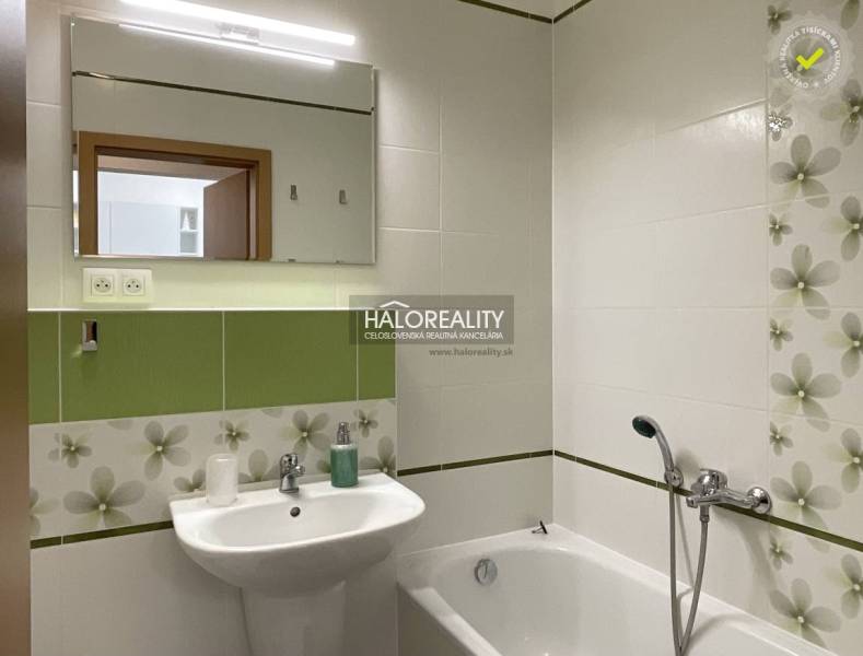 A bathroom with green and white tiles, a bathtub, and a sink, suitable for a studio apartment.