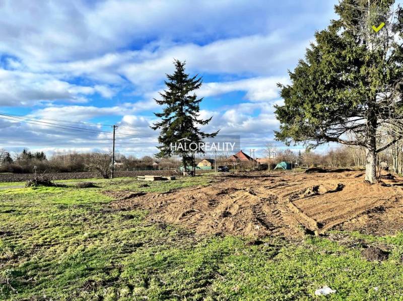 Residential plots in Ondrejovce with grassy areas and trees under a blue sky.