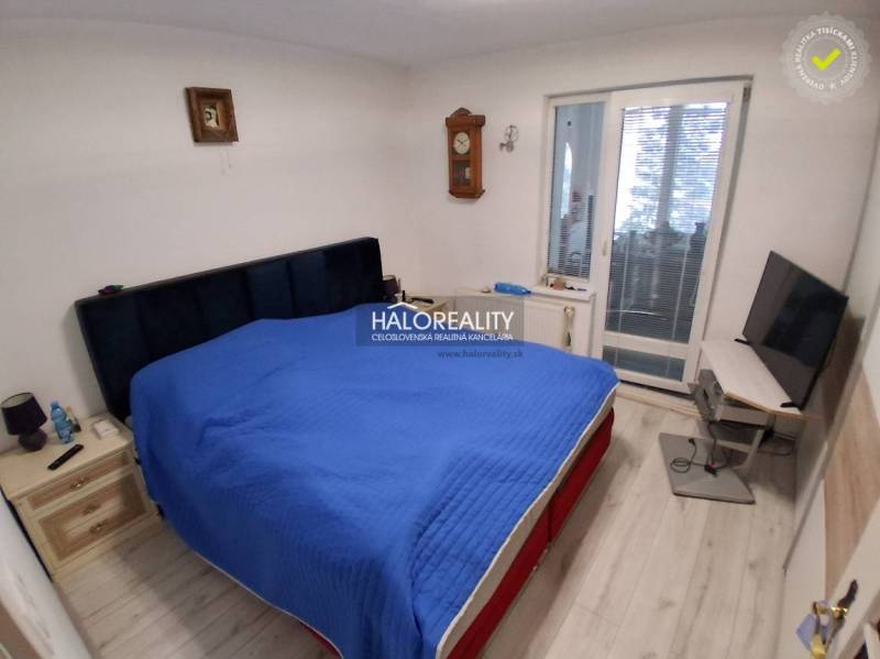 A bedroom with a bed, a television, a wooden floor, and balcony doors in a family house.
