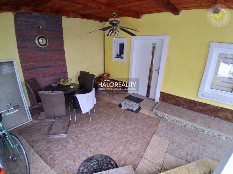 The terrace of the family house with tiles and seating furniture. In the alcove, there is a table and a clock.