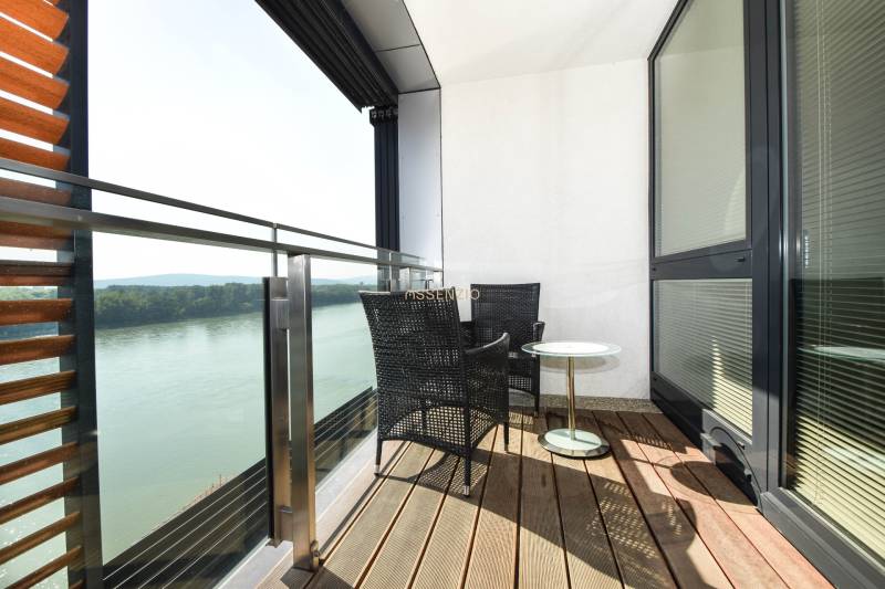 Balcony with a view of the river, two chairs, a table, wooden floor decor.