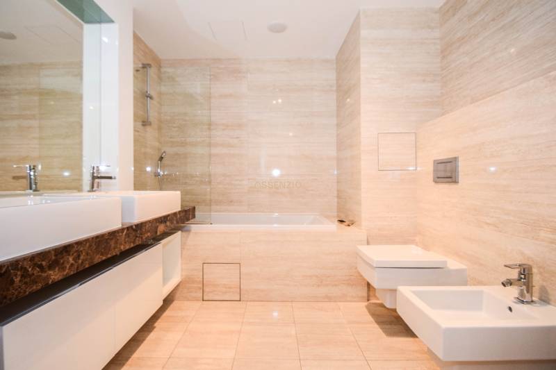 Bathroom with a bathtub, bidet, and double sink in a 3-room apartment. Light tiles dominate the space.