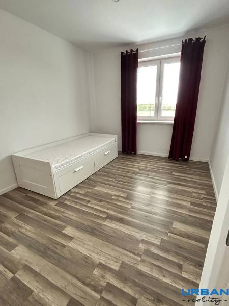 A room with a bed, a wooden floor decor, and a large window in a 3-room apartment.