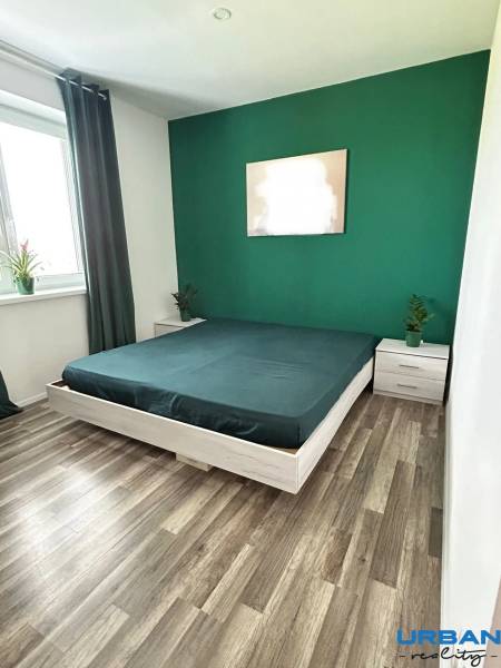 Bedroom in a 3-room apartment with a wooden decor floor; green wall, bed, window.