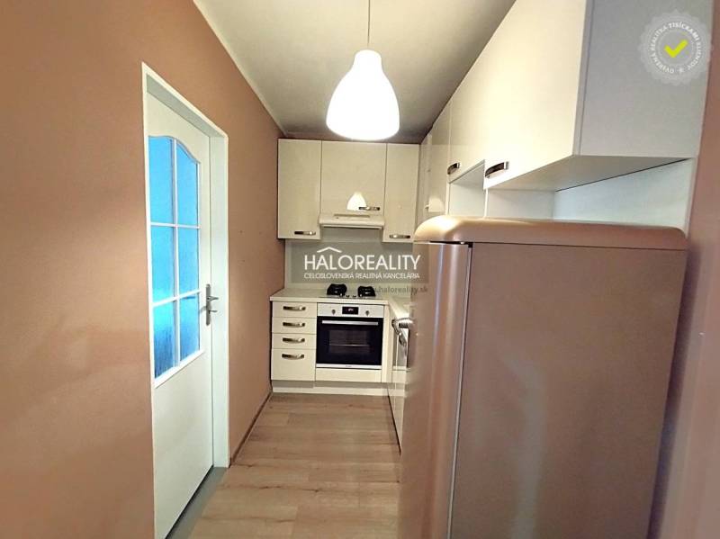 A kitchen in a 2-room apartment with a compact kitchenette, wooden decor flooring, and a refrigerator.